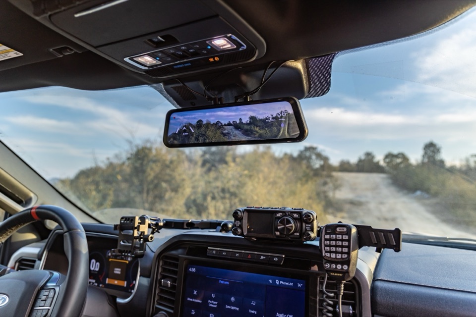 A Wolfbox mirror-style dash camera installed in a truck, showing the road ahead on its wide display